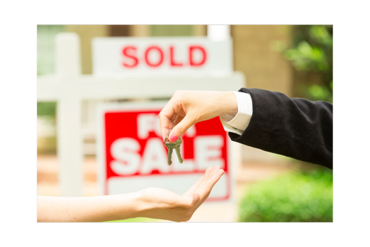 Real estate agent handing over house keys in front of a SOLD sign